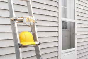 Picture of a ladder, work gloves, and a hard hat leaning against new vinyl siding.